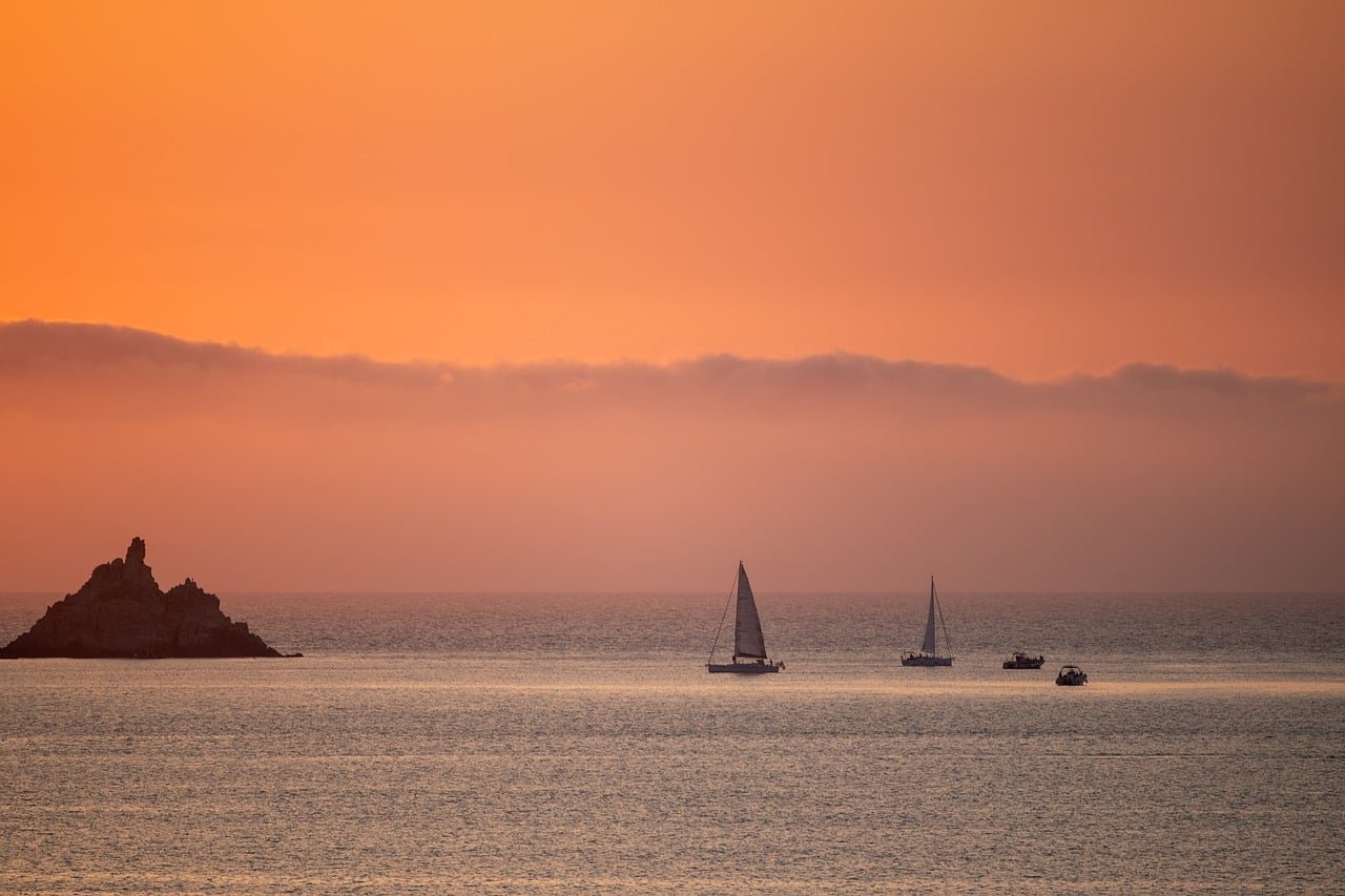 Atardecer mediterr&aacute;neo en Calvi, C&oacute;rcega, con barcos y costa, ideal para fondo de pantalla.