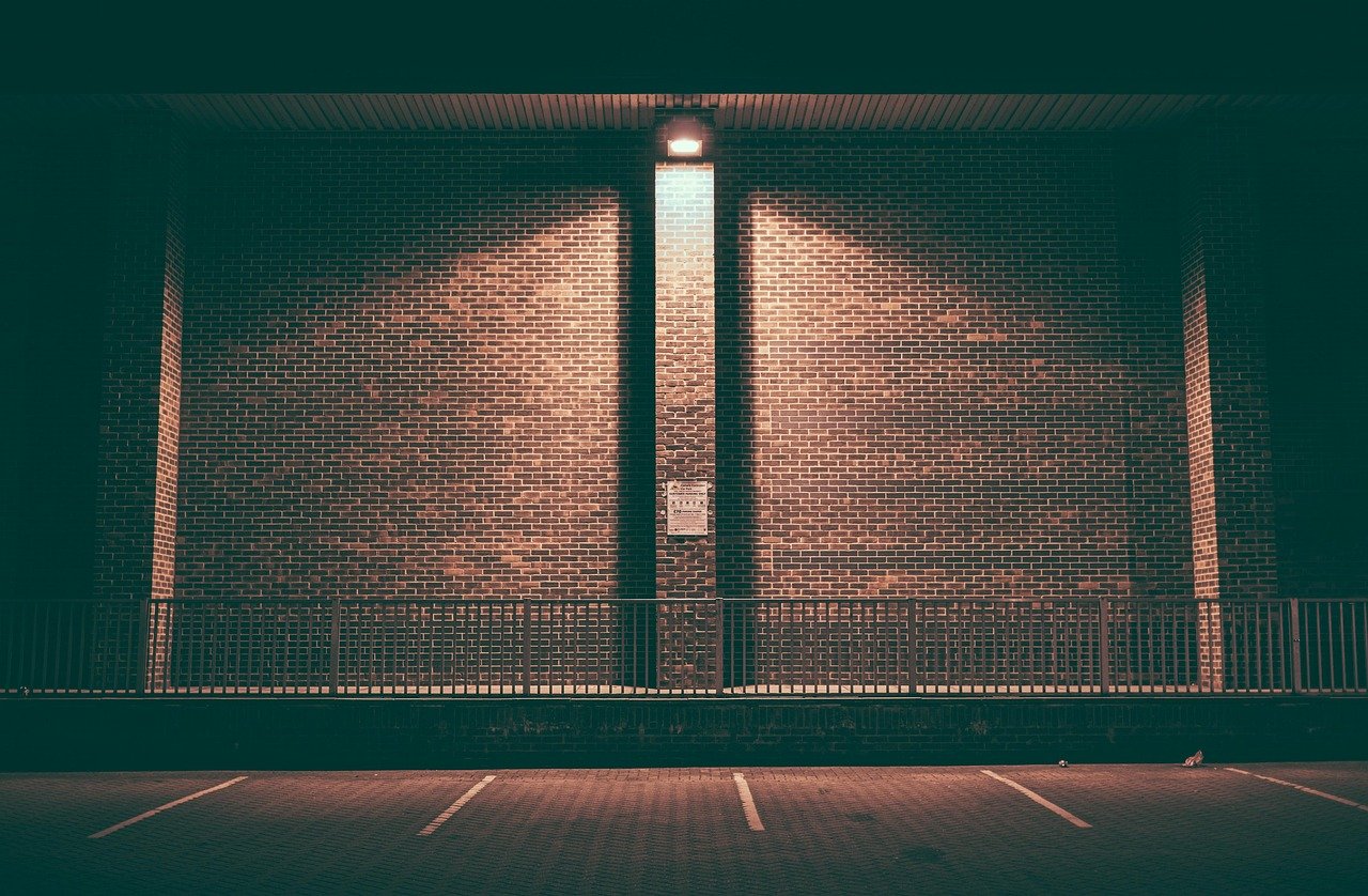 Muro de ladrillo vacío e iluminado de noche en un aparcamiento con barandilla de acero.