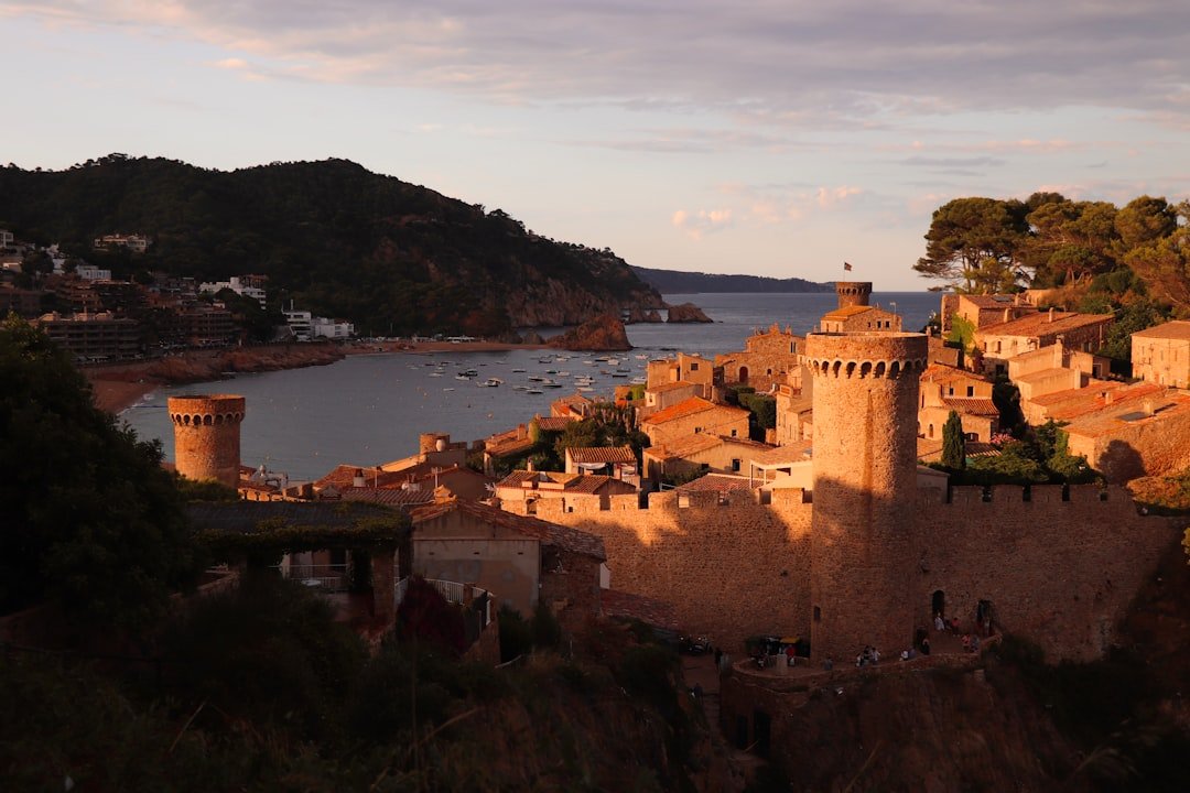 Tossa de Mar al atardecer: castillo medieval ic&oacute;nico en la Costa Brava, Catalu&ntilde;a, con barcos pesqueros.