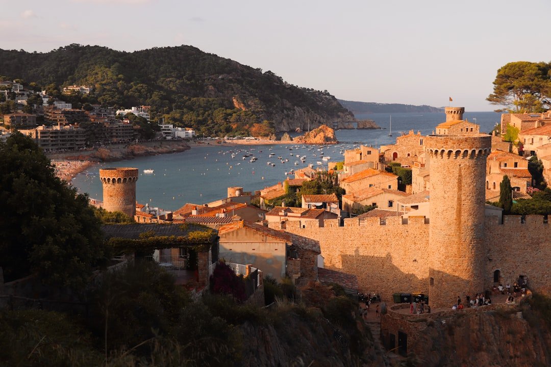 Tossa de Mar al atardecer: torres medievales, murallas, bah&iacute;a con barcas y tejados terracota.