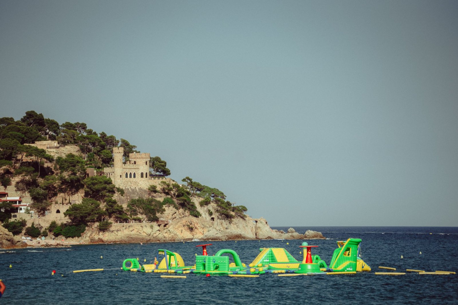 Castillo historico en colina rocosa junto a parque acuatico inflable en el mar.