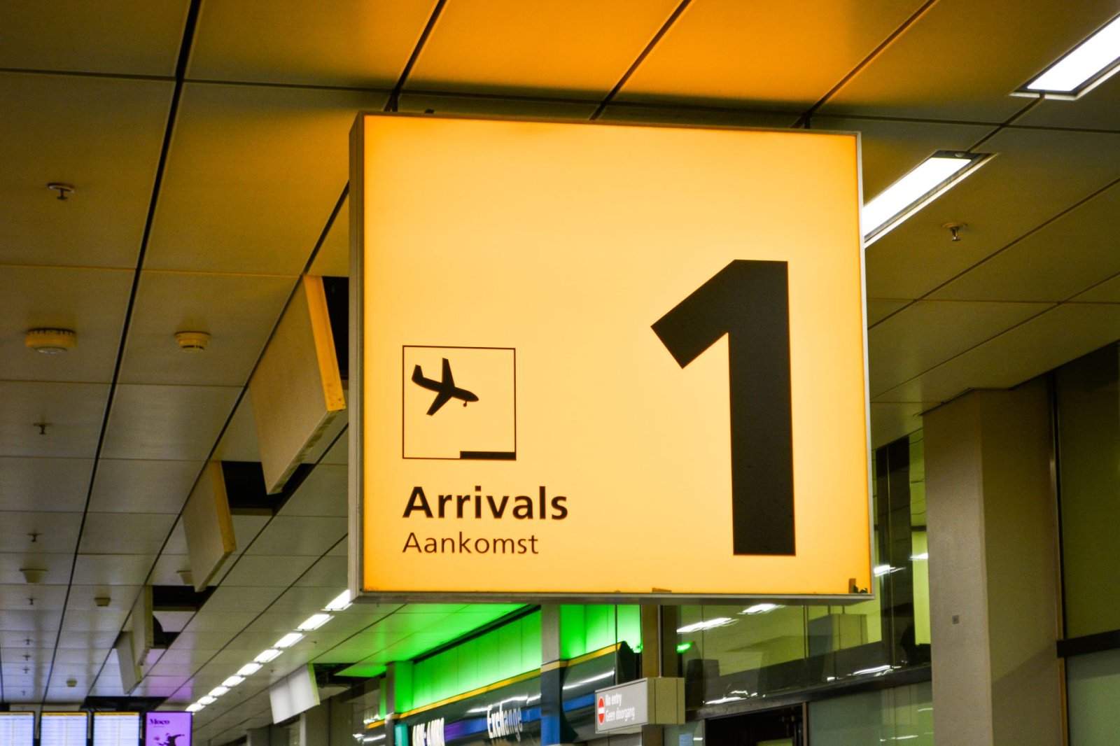 Leuchtendes Ankunftsschild mit Flugzeugsymbol am Flughafenterminal.